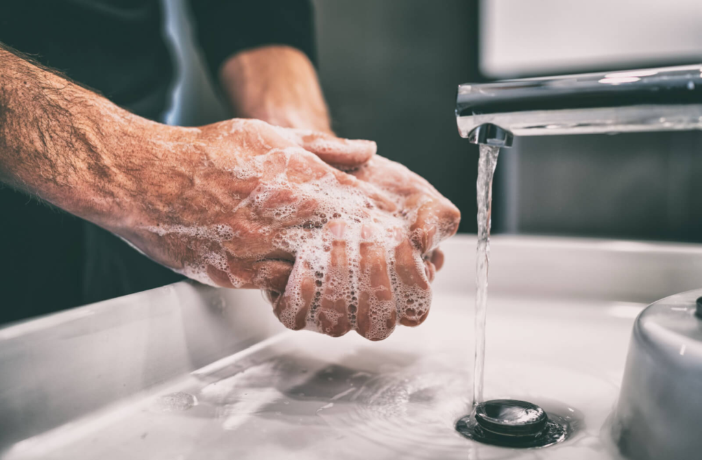 A man washing his hands in a sink using soap and running water before cleaning his glasses.