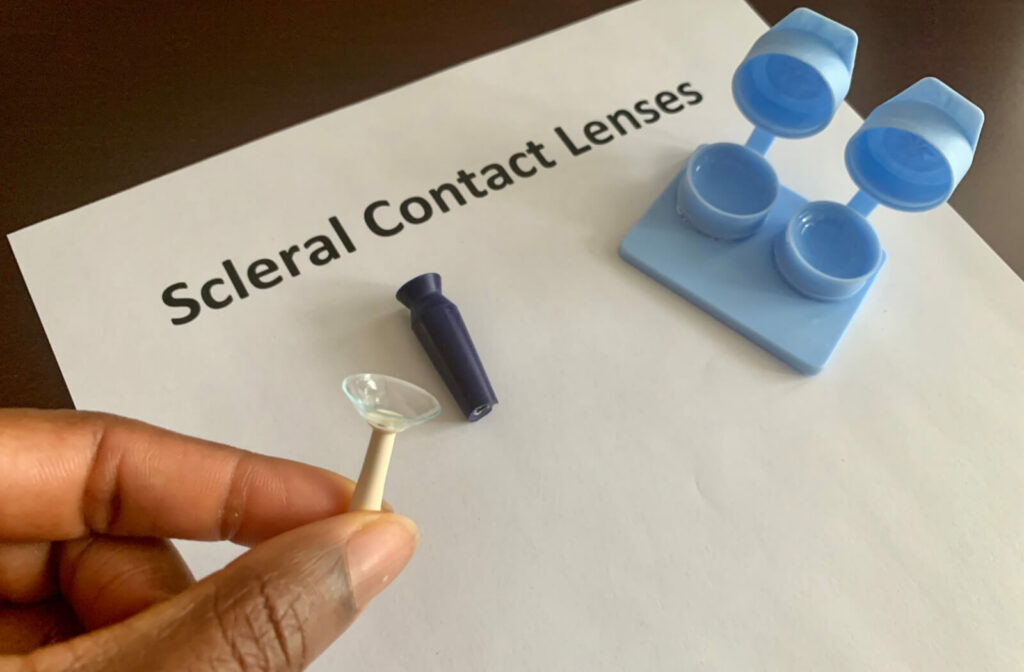 A kit containing scleral contacts and a hand holds a tool for inserting and removing contact lenses.