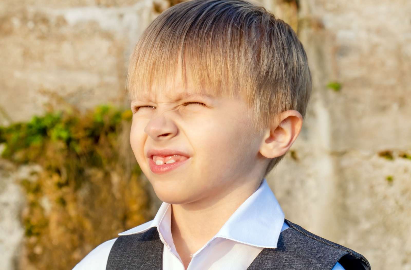 A boy squinting his eyes from the bright sun outdoors.
