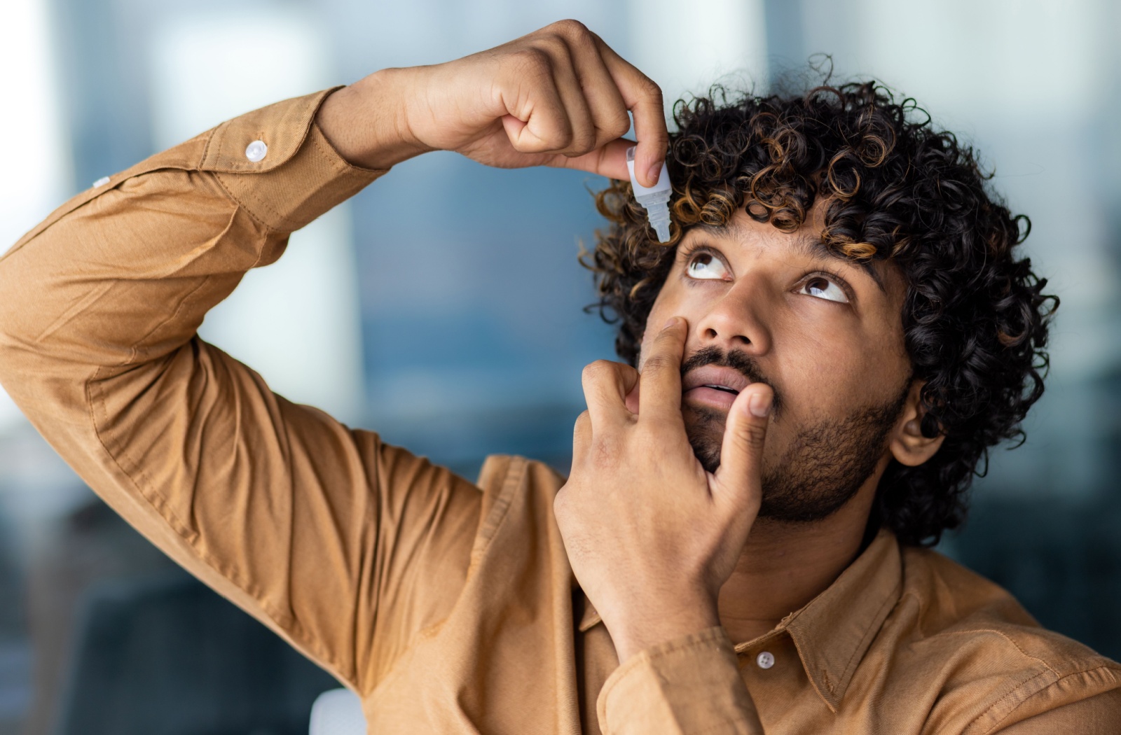 An adult places contact-safe eye drops into their eye, following proper administration instructions.
