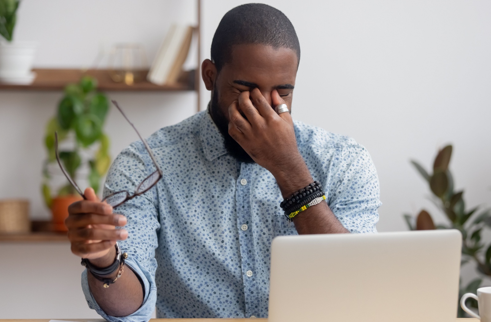 An office worker removes their eyeglasses to rub their tired eyes after working on the computer all day