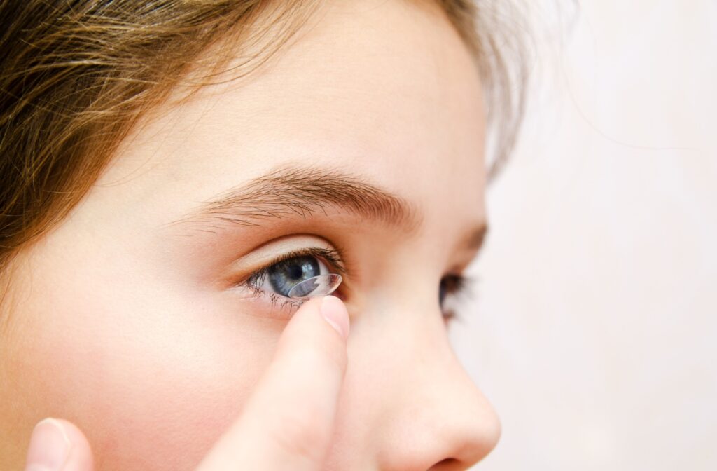 A close-up image of a young child carefully putting a contact lens into their right eye.