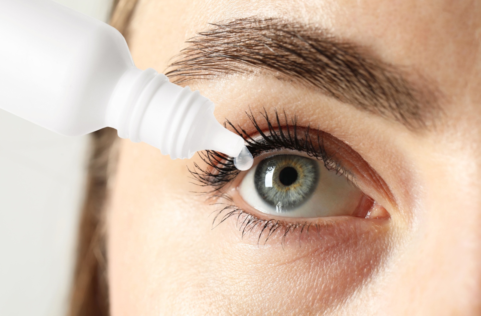 A close-up image of a person dropping an eye drop into their eye for relief.
