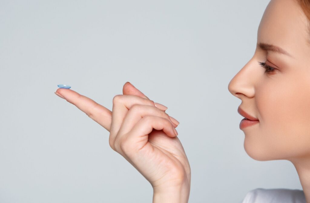A patient smiling while holding a contact lens on the tip of their left index finger in front of a gray background.