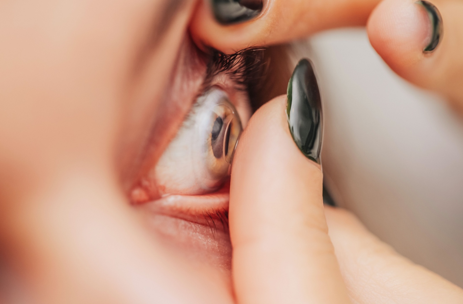 A close-up of a finger carefully inserting a contact lens onto a person's eye.