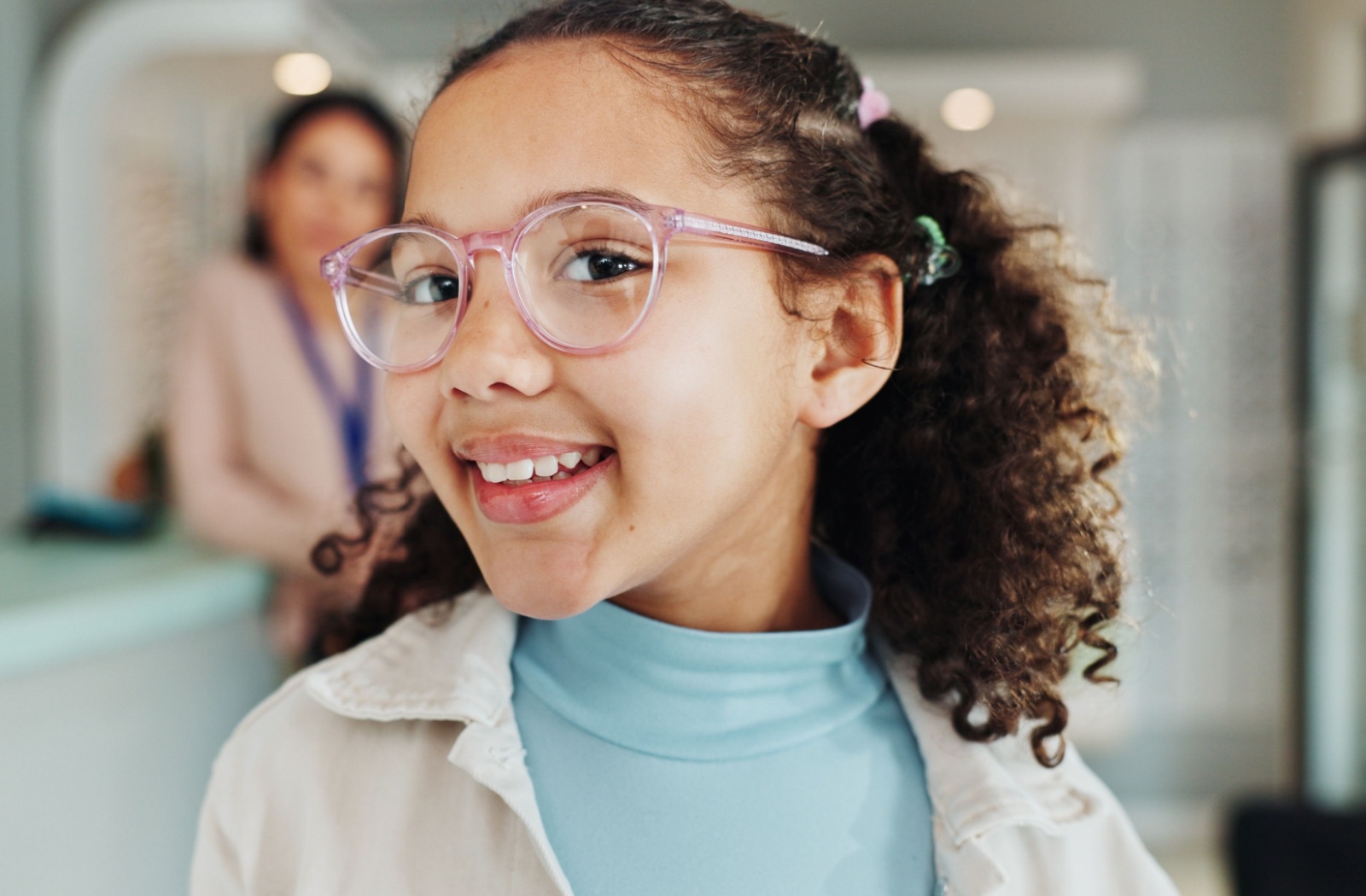 Child looks to the side while wearing glasses and smiles at her reflection
