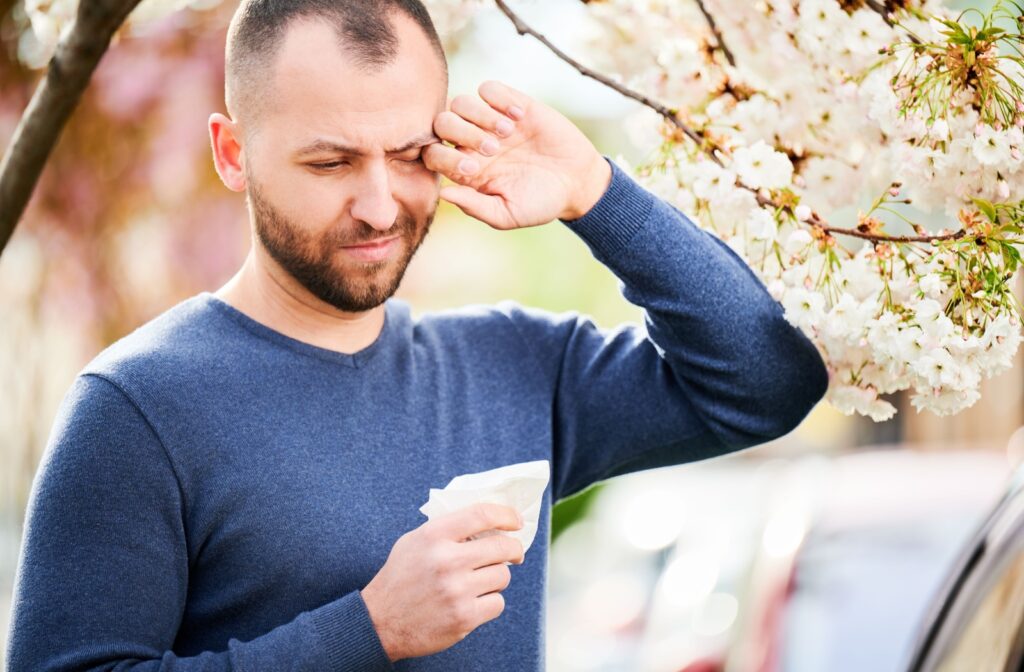 A person outside with a tree rubbing their eye