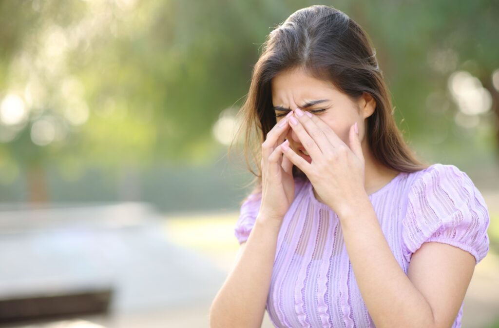 A person rubbing their eyes while outside because they are experiencing eye allergies