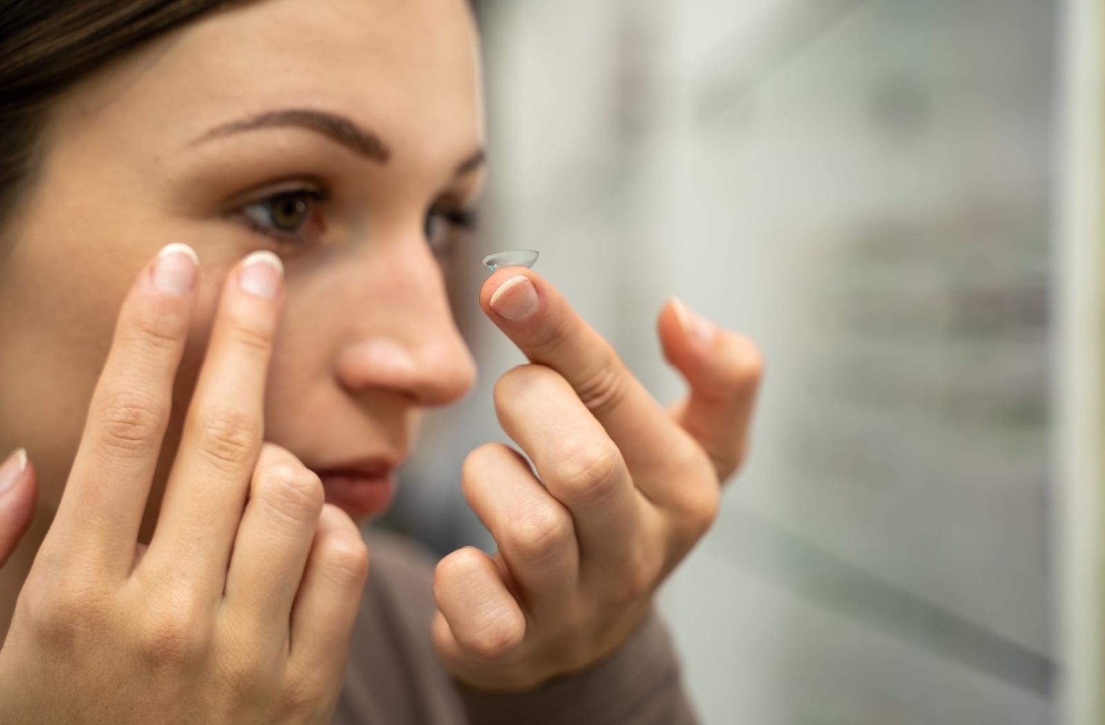 A person looking at a contact lens on their finger that they are about to put in to their eye.