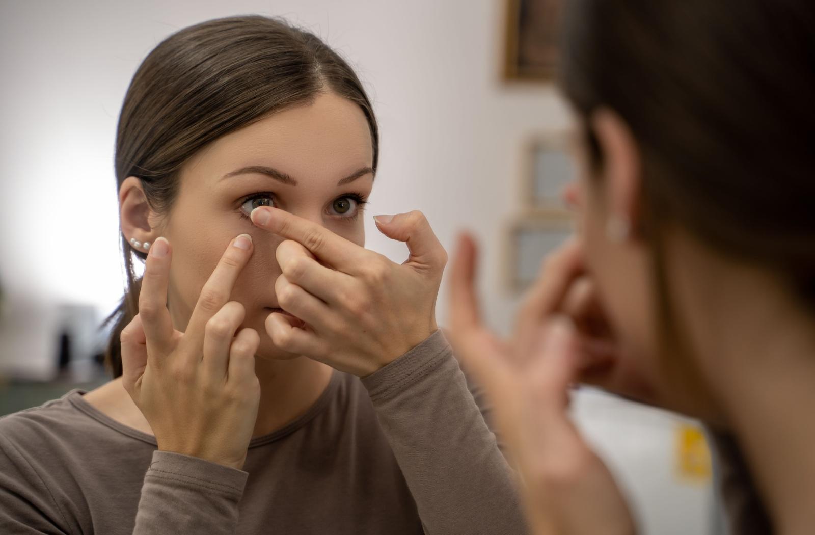 A person putting a contact lens in their eye while looking in a mirror